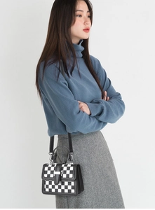 Detailed side view of houndstooth crossbody bag with metallic clasp and leather handle