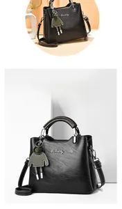 Close-up of black oily wax leather tote with silver metal logo and green doll charm detail
