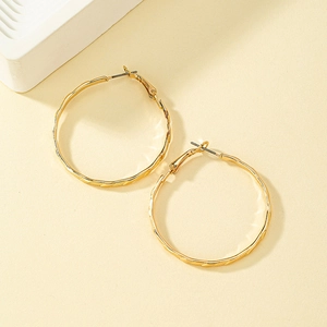 Boucles d'oreilles créoles dorées à texture torsadée sur fond beige chaud élégant