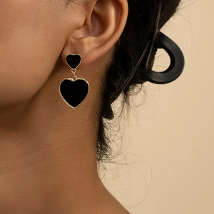 Gros plan de boucles d'oreilles cœur asymétriques en or et émail noir sur modèle