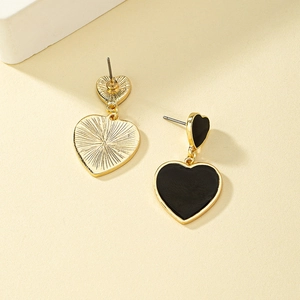 Vue macro de boucles d'oreilles cœur asymétriques dorées avec émail noir et dos texturé