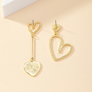 Détail de boucles d'oreilles cœur dorées asymétriques avec design ajouré et texture