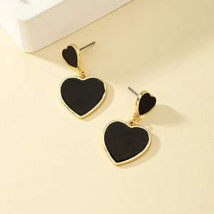Détail de boucles d'oreilles double cœur asymétriques en émail noir et finition dorée