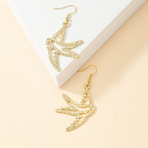 Detail shot of gold swallow earrings with textured hammered finish on white stone stand