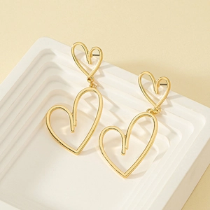 Gros plan sur des boucles d'oreilles cœur creux asymétriques plaquées or sur support blanc