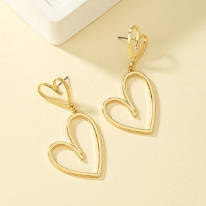 Détail de boucles d'oreilles cœur évidé asymétriques dorées sur fond beige texturé
