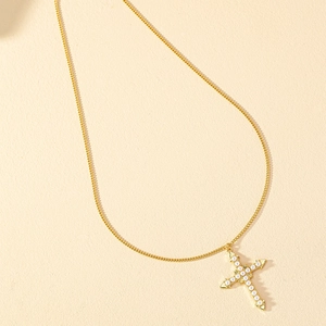 Élégant collier doré avec pendentif en croix orné de perles blanches sur fond texturé