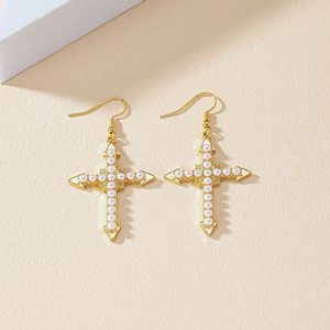 Elegant gold-plated cross earrings with white faux pearl inlay on beige background