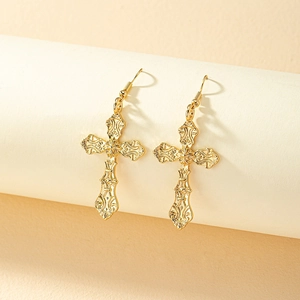 Detail shot of vintage golden cross earrings with baroque embossed patterns on a stand