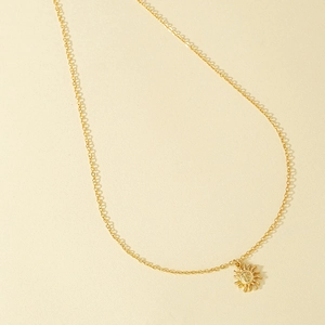 Minimalist gold sun pendant necklace with radiant texture on a matte beige background