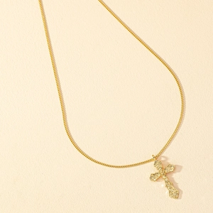 Macro detail of golden cross pendant featuring intricate vintage baroque floral patterns