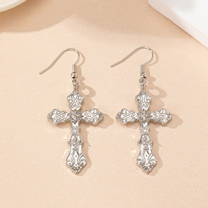 Macro detail of silver cross earrings with intricate Baroque floral engraving texture
