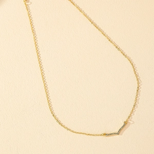 Minimalist gold V-shaped pendant necklace with sparkling zircons on a beige background