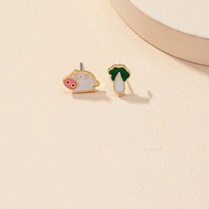 Détail de boucles d'oreilles asymétriques cochon et chou sur fond crème minimaliste