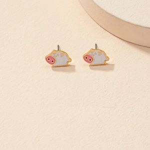 Gros plan de boucles d'oreilles cochon en émail blanc avec nez rose et base dorée