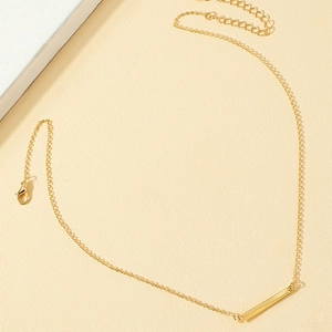 Minimalist gold necklace with a polished bar pendant on a textured beige surface