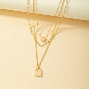 Dreilagige goldene Halskette mit Herz- und Schlossanhängern auf strukturiertem Grund