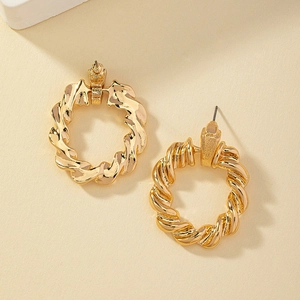 Boucles d'oreilles créoles dorées torsadées avec un design en spirale sur fond beige