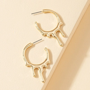 Boucles d'oreilles dorées en forme de lave fluide sur un fond beige minimaliste