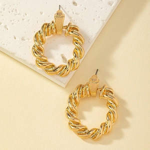 Boucles d'oreilles créoles torsadées dorées avec design spirale sur fond de pierre blanche