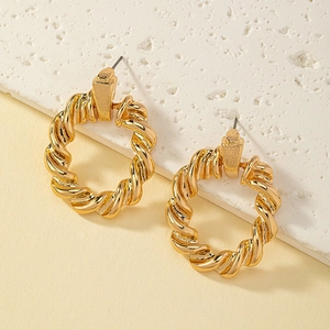 Détail de boucles d'oreilles créoles torsadées dorées avec texture en spirale sur pierre