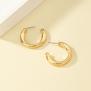 Minimalist chunky gold C-shaped earrings with a polished finish on textured background
