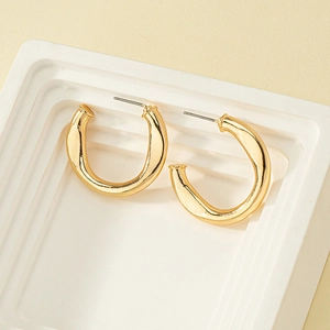 Close-up of chunky gold-tone twisted earrings on a minimalist white stone tray display