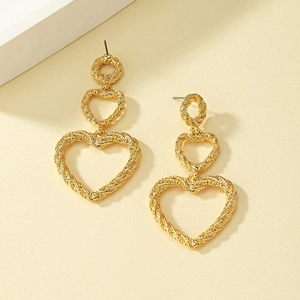 Détail de boucles d'oreilles cœur dorées avec texture corde torsadée et design étagé