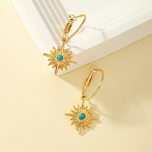 Créoles dorées avec pendentif soleil et pierre turquoise sur fond beige texturé élégant