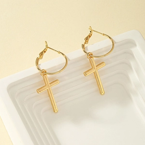 Détail de boucles d'oreilles créoles croix dorées sur supports géométriques
