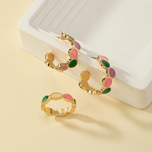 Macro detail of gold-plated enamel C-hoop earrings and matching wave-edge ring set