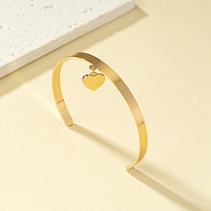 Elegant gold flat open bangle with a polished heart pendant on a minimalist background