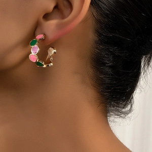 Detail of gold C-shaped clip-on earrings with pink, green and purple enamel inlay