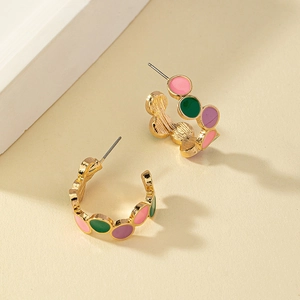 Detail of C-shaped gold-plated earrings featuring colorful enamel dots in pink and green