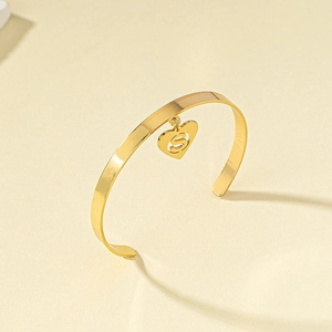 Detail of gold heart charm bangle featuring a cutout letter S on minimalist jewelry