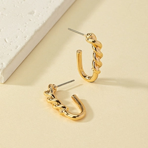 Macro view of gold-plated alloy twisted hoop earrings on a textured stone tray