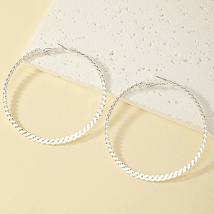 Macro detail of silver twisted hoop earrings resting on a textured white stone background