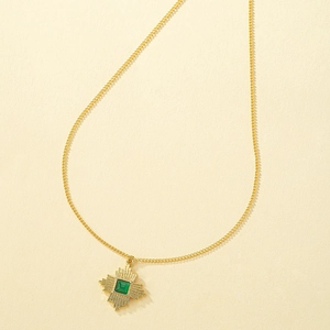 Detail of a vintage golden necklace featuring a geometric pendant with a green gemstone