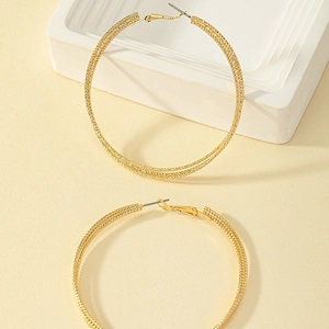 Macro detail of large gold hoop earrings with intricate woven texture and latch-back closure