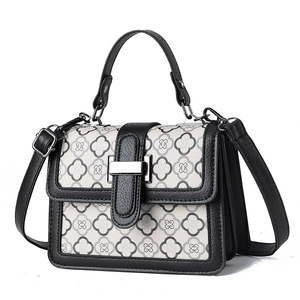 Quilted off-white handbag with clover pattern and black adjustable strap on white background