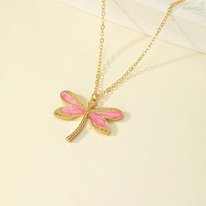Collana con libellula dorata ed ali in smalto rosa su sfondo bianco caldo