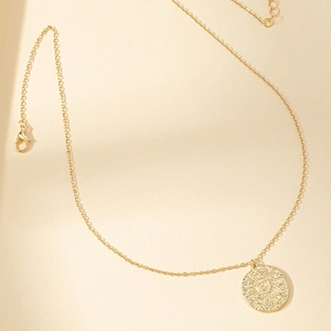 Macro view of gold sun coin pendant necklace with a vintage embossed face detail
