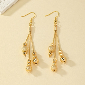 Détail de boucles d'oreilles pampilles dorées avec perles mates et polies sur fond beige