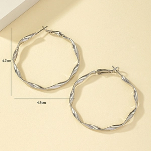 Détail de créoles torsadées argentées d'un diamètre de 4,7 cm dans un style minimaliste