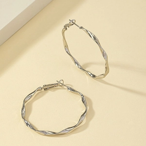 Boucles d'oreilles créoles torsadées argentées au design ondulé sur fond beige