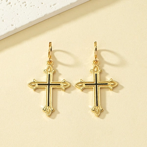 Détail de boucles d'oreilles croix dorées avec émail noir et textures vintage gaufrées