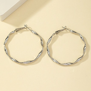 Boucles d'oreilles créoles torsadées argentées avec finition métallique polie sur fond beige