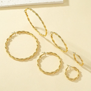 Detailed set of three golden twisted hoop earrings in various sizes on a stone background