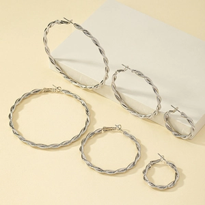 Five sizes of silver twisted rope hoop earrings displayed on white minimalist platforms