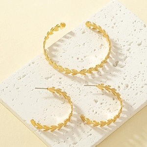 Detail shot of golden olive leaf bracelet and hoop earrings set on a stone platform